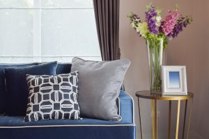 A blue couch with pillows and a vase of flowers.